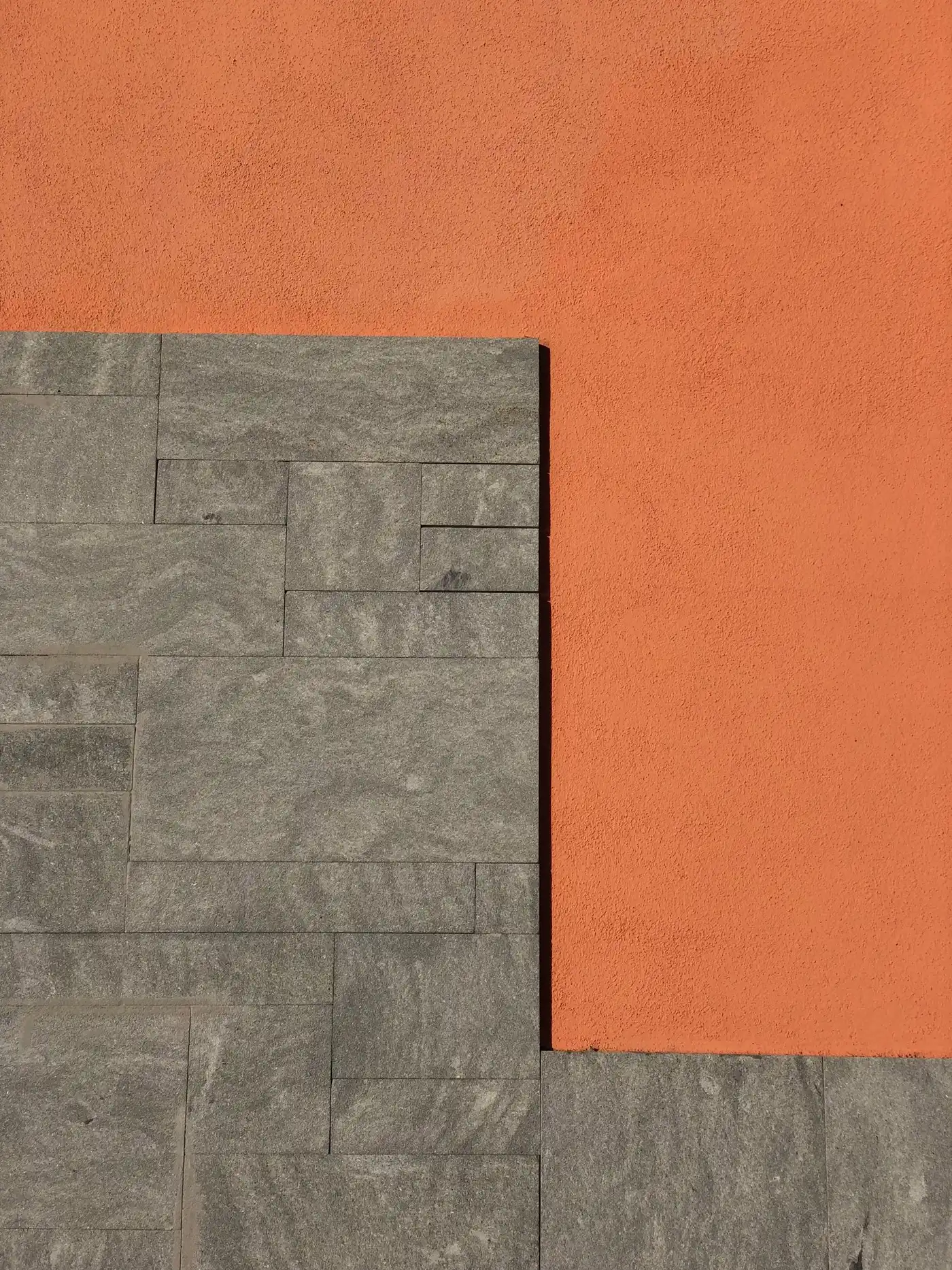 A flat orange wall meeting grey stone blocks in a sharp L-shaped line