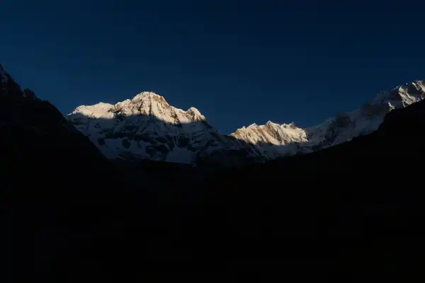 Snow peaks catching the first sun above a valley still in deep shadow