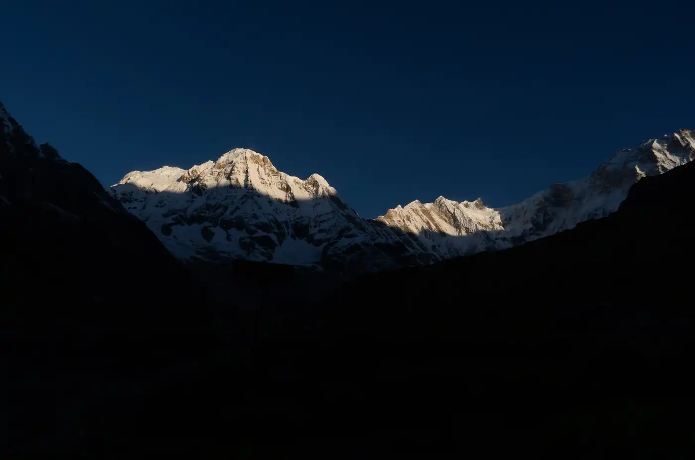 Snow peaks catching the first sun above a valley still in deep shadow