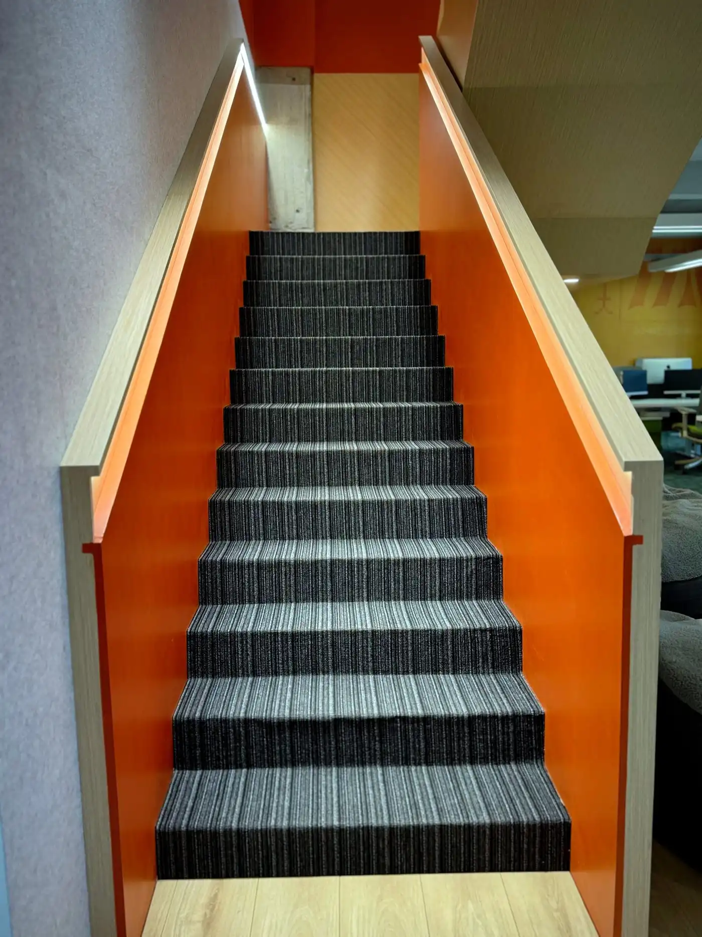 A straight staircase with grey striped treads between bright orange walls, seen from the bottom