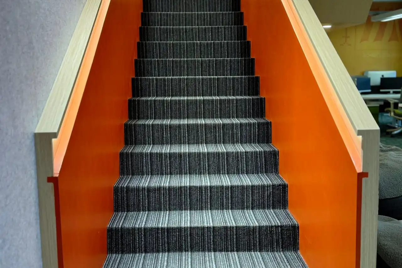 A straight staircase with grey striped treads between bright orange walls, seen from the bottom