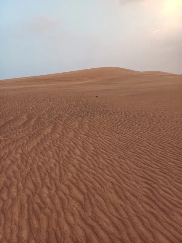 A rust-red desert dune with fine wind ripples under a hazy sky