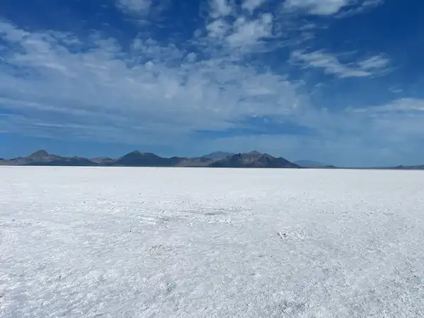 A white salt flat stretching to low blue mountains under a sky of scattered clouds