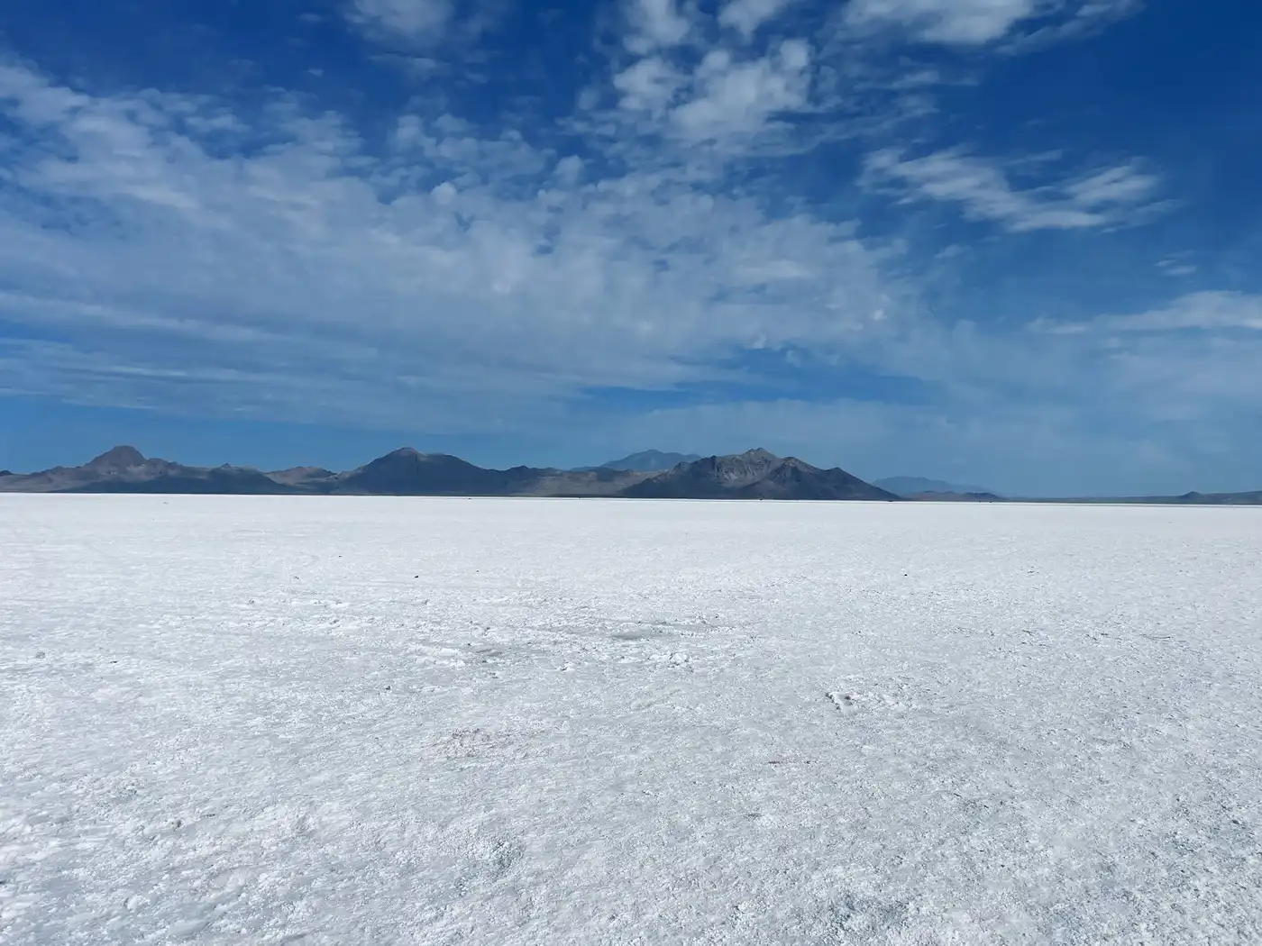 A white salt flat stretching to low blue mountains under a sky of scattered clouds
