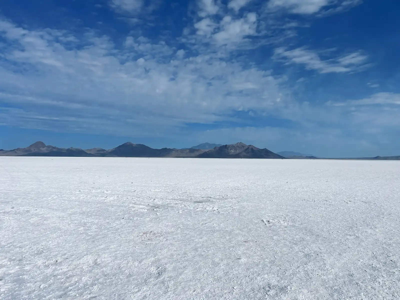 A white salt flat stretching to low blue mountains under a sky of scattered clouds