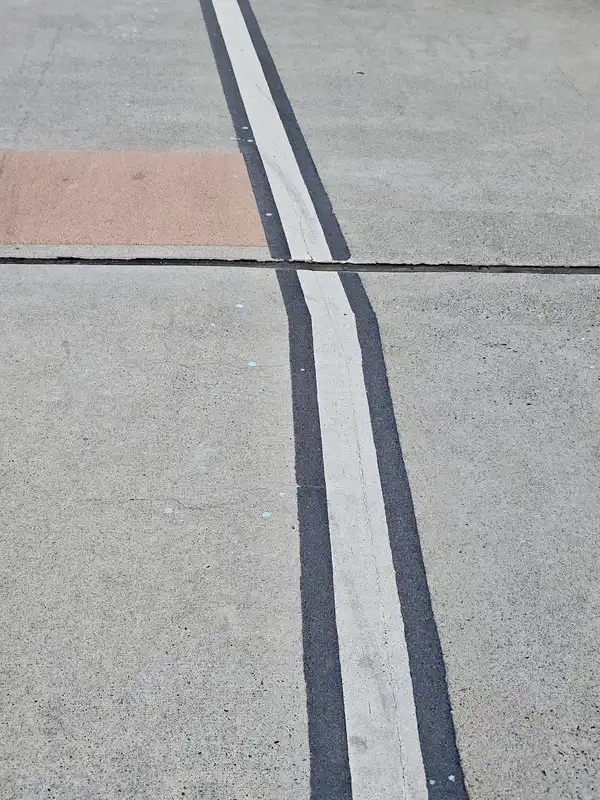 Two parallel white lines on grey pavement, with one square of red brick