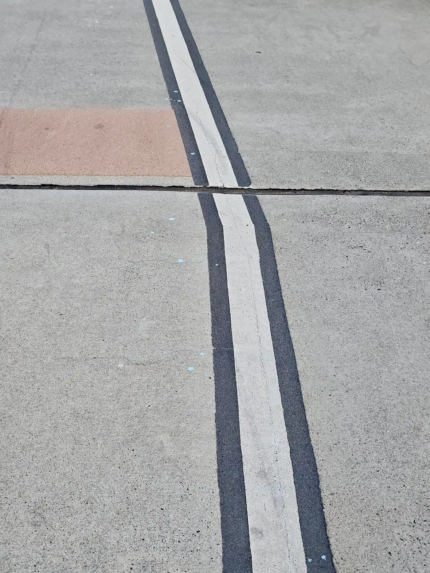 Two parallel white lines on grey pavement, with one square of red brick